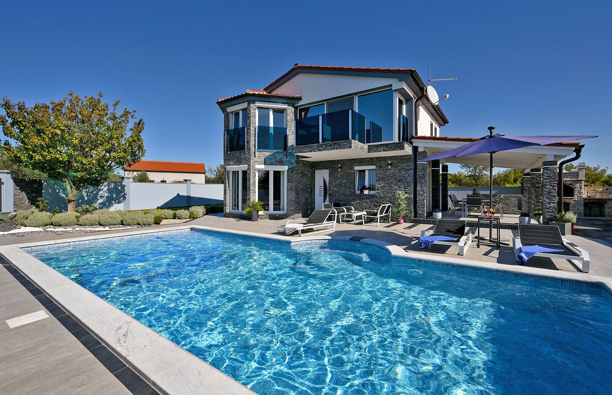 A modern two-story house with a swimming pool, outdoor seating, and a stone facade.