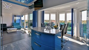 A modern kitchen with a blue island, large windows, and a view of the outdoors.