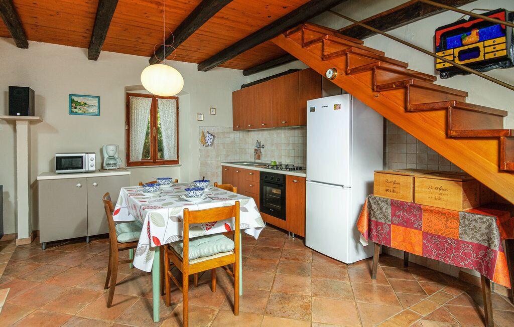 A kitchen with wooden cabinets, a white refrigerator, a dining table with chairs, and a staircase.