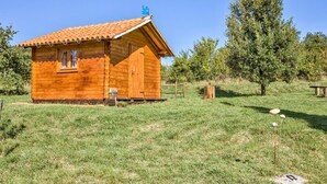 A wooden cabin with a tiled roof, a small porch, and a grassy field with trees in the background. - House 1974 (Barban)