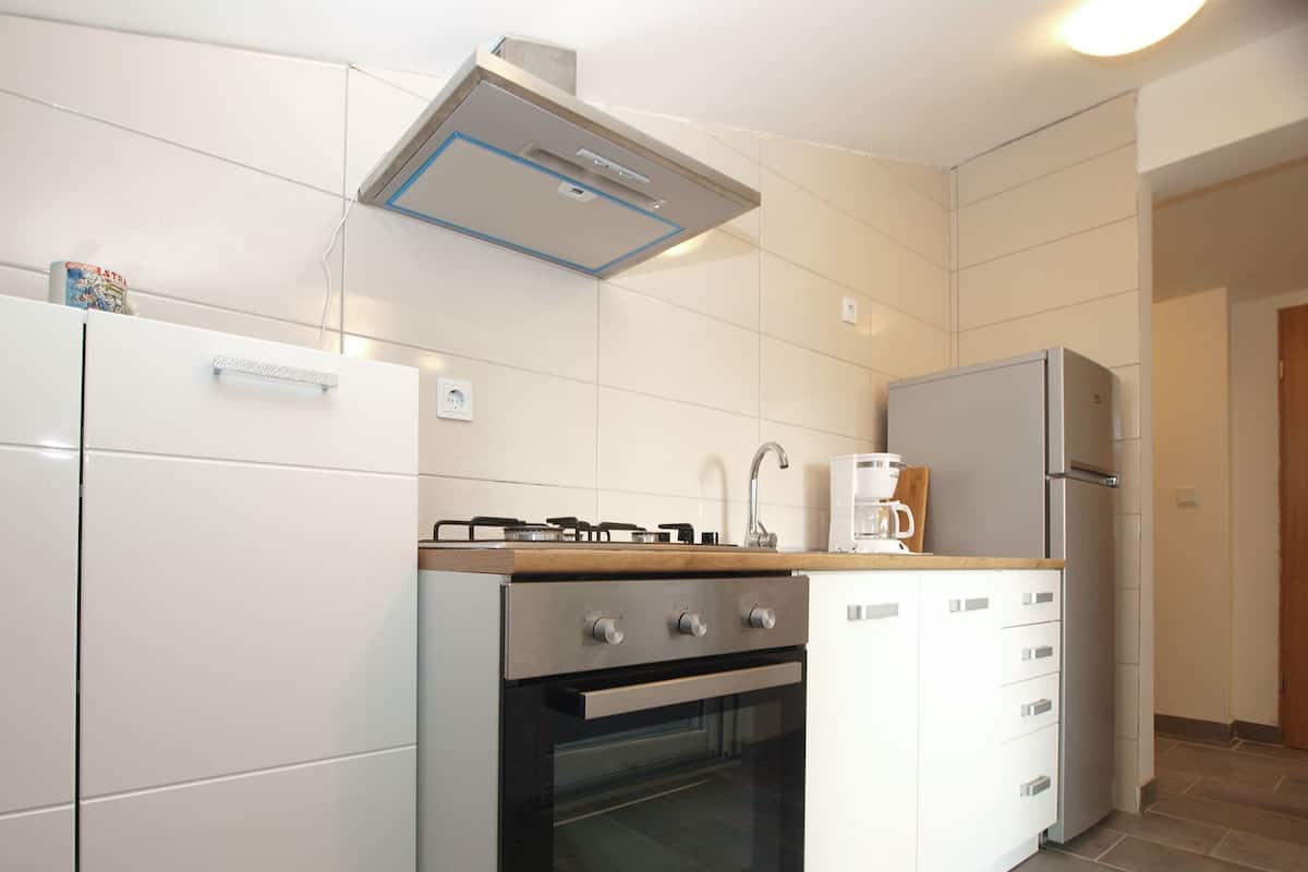 A modern kitchen with white cabinetry, a built-in oven, a gas stove, a coffee maker, and a refrigerator.