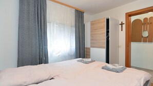 A bedroom with a bed, a wardrobe, a cross on the wall, and a door with a wooden frame. - Apartment 1976 (Vodnjan)