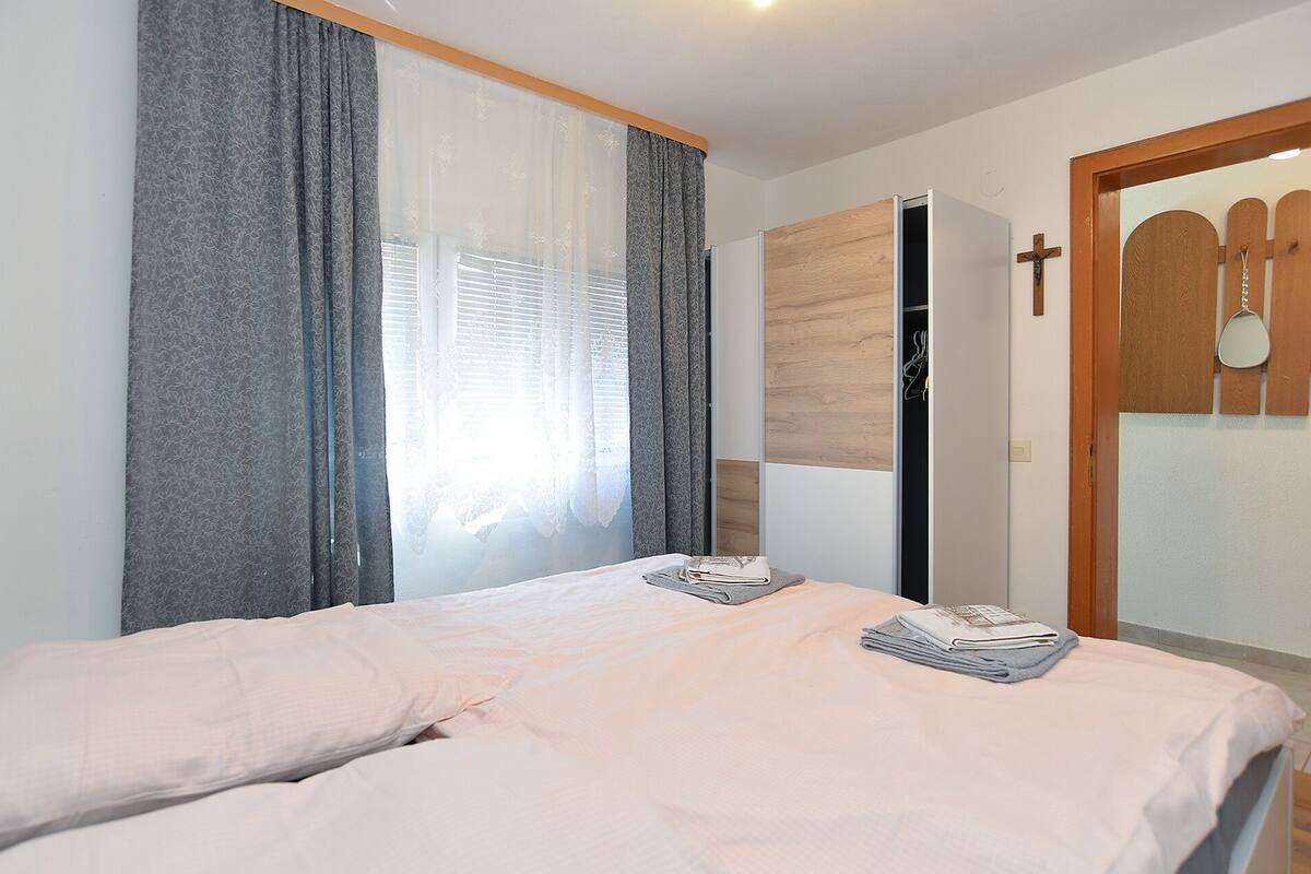 A bedroom with a bed, a wardrobe, a cross on the wall, and a door with a wooden frame.
