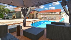An outdoor pool area with wicker furniture, a covered seating area, and a view of buildings in the background. - Apartment 1976 (Vodnjan)