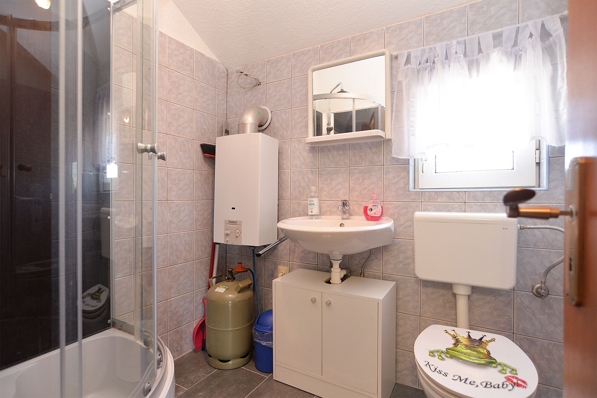 Ein Badezimmer mit Dusche, Toilette, Waschbecken und Gasflasche.