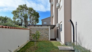 A small courtyard with a stone wall, a grassy area, and a building with a tiled roof. - Apartment 1977 (Medulin)