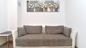 A living room with a brown textured sofa, a small white side table, and a large abstract painting on the wall. - Apartment 1977 (Medulin)