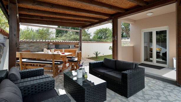 An outdoor patio with a wooden table and chairs, a black sofa, and a glass door leading to a covered area. - Apartment 1977 (Medulin)