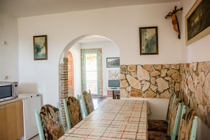 A dining area with a long table and chairs, a stone wall, and a crucifix on the wall.