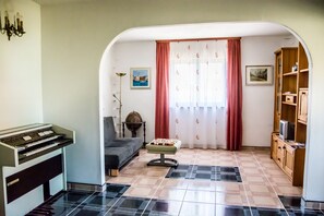 A living room with a piano, a sofa, a small table, a lamp, and a bookshelf.