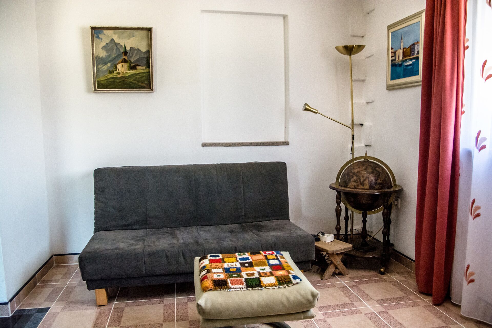 Una sala de estar con un sofá gris, una mesita con una lámpara y un cojín colorido.