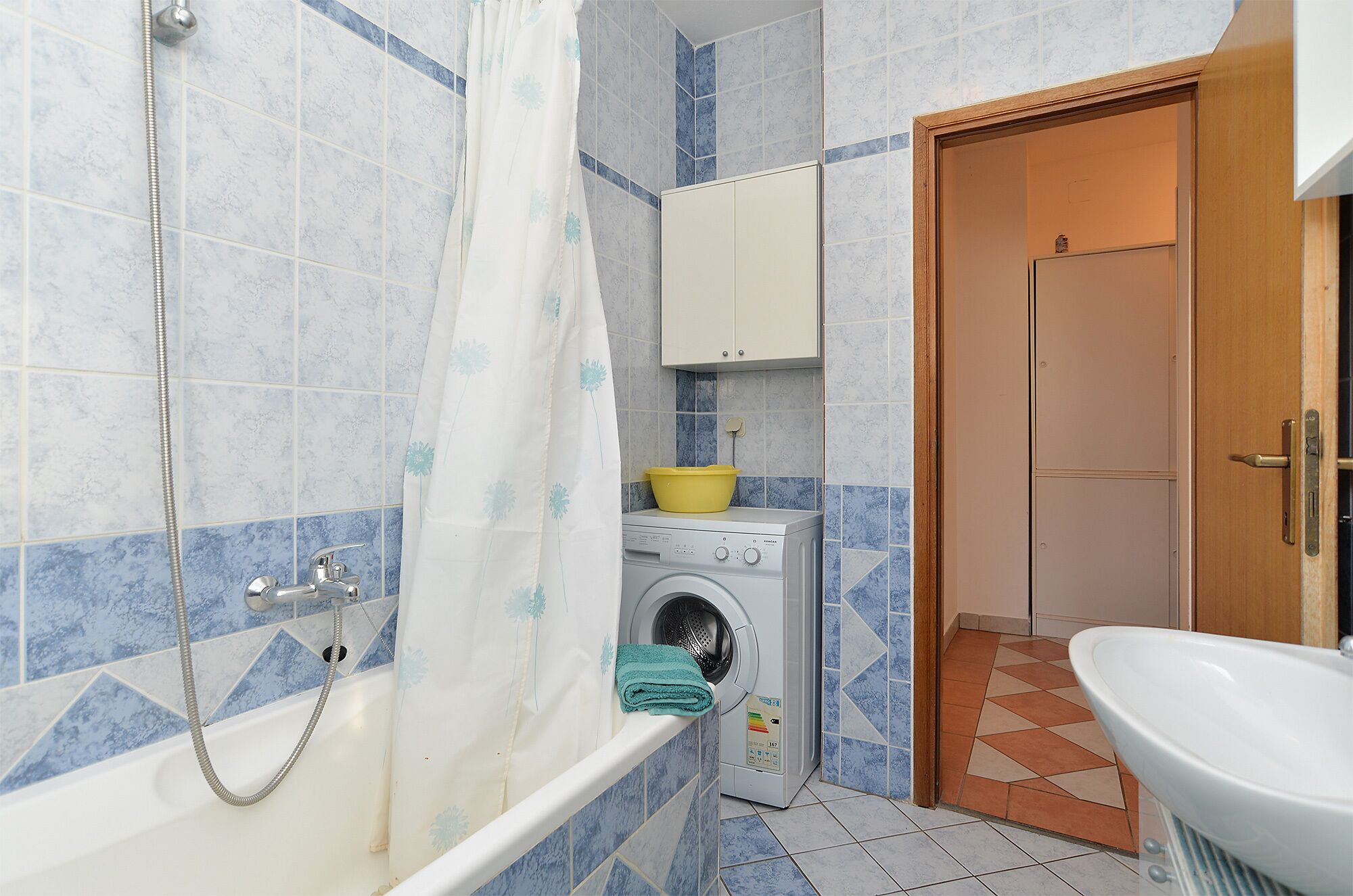A bathroom with a shower, a washing machine, a sink, and a cabinet.