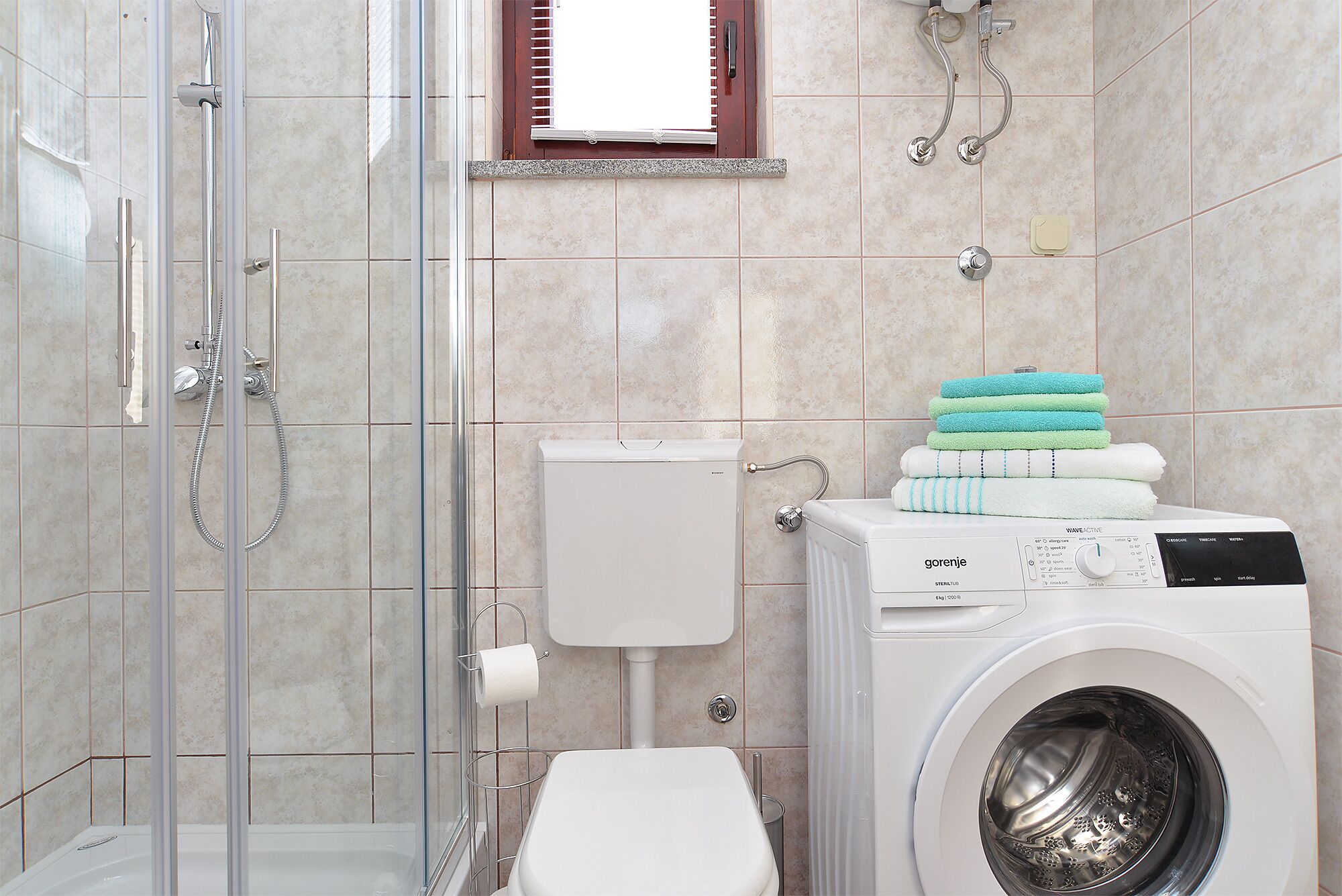 A bathroom with a glass-enclosed shower, a toilet, and a front-loading washing machine.