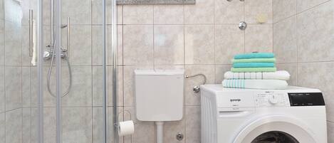 A bathroom with a glass-enclosed shower, a toilet, and a front-loading washing machine.