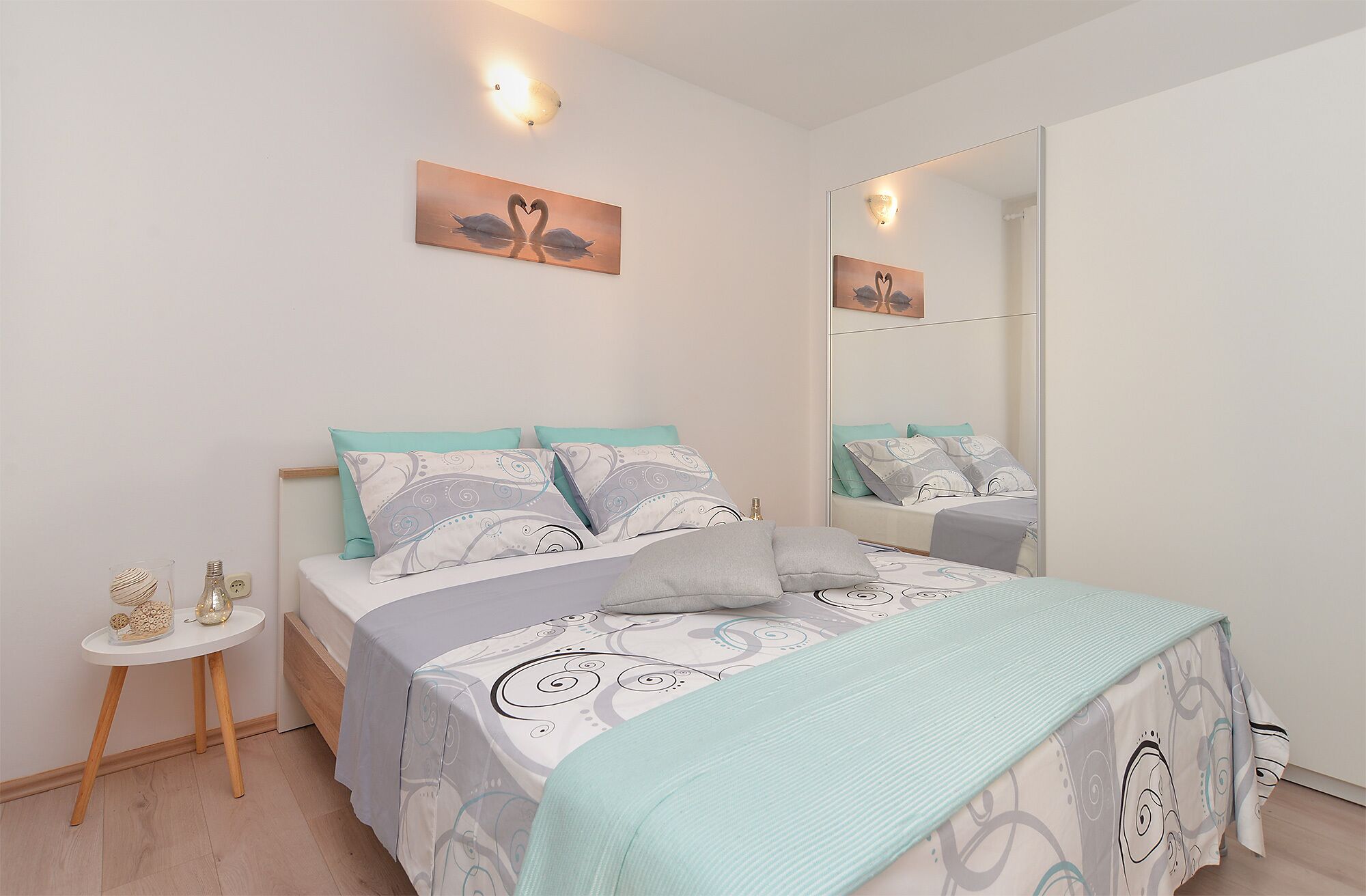 Un dormitorio con cama, mesita de noche, espejo y decoración en la pared.
