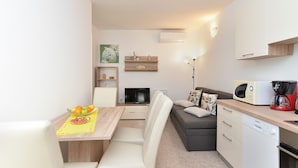 A compact living space with a dining area, a sofa, a TV, a microwave, and a coffee maker. - Apartment 1983 (Fazana)