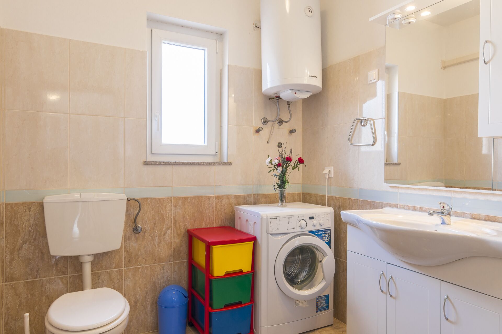A bathroom with a toilet, a washing machine, a sink, and a mirror.