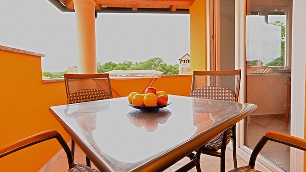 Un balcón con mesa y sillas, un frutero y vista a zonas verdes y un edificio al fondo.