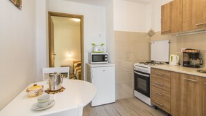Una cocina compacta con una mesa blanca, un microondas, un refrigerador pequeño, una estufa y armarios de madera.