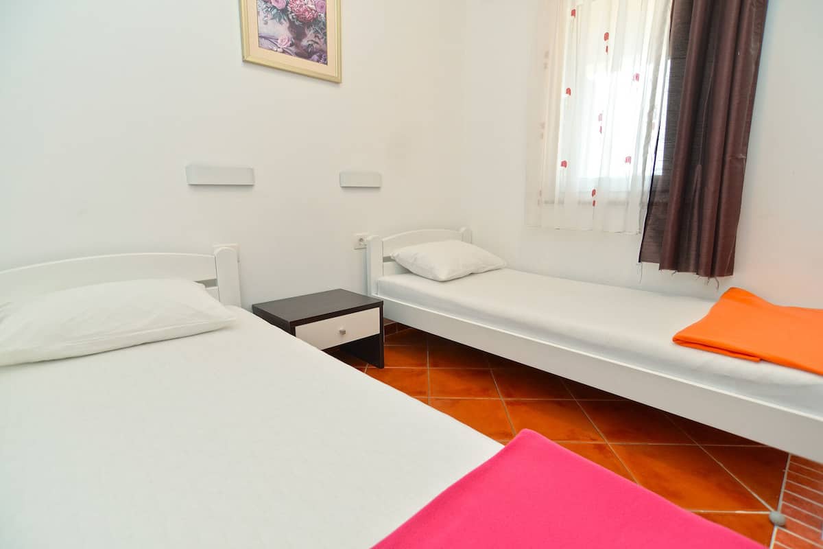 A small, clean room with two single beds, a nightstand, a small table, and a window with curtains.
