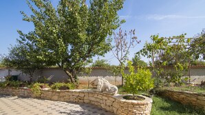 Un sendero de piedra que lleva a un jardín con una estatua de un caballo, rodeado de vegetación y un cielo despejado.