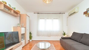 A modern living room with a grey sofa, a glass coffee table, wooden shelves, and a TV on a wooden cabinet. - Apartment 1987 (Pula)