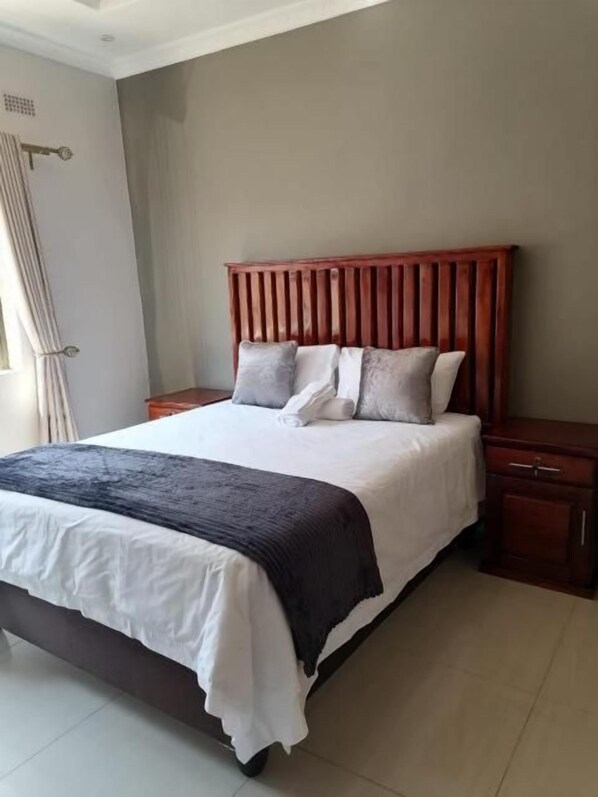 A bedroom with a bed, a nightstand, and a wooden headboard. - 848 Guest House (Victoria Falls)