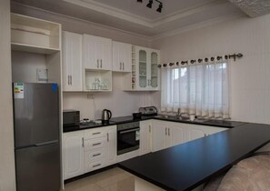 A modern kitchen with white cabinetry, a black countertop, and a stainless steel refrigerator. - 848 Guest House (Victoria Falls)