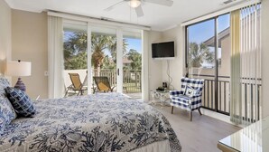 Ein Schlafzimmer mit Bett, Fernseher, Balkon mit Stühlen und Deckenventilator.