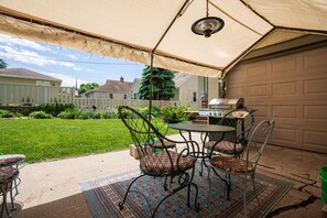 Una veranda coperta con tavolo e sedie, un barbecue e un garage sullo sfondo.