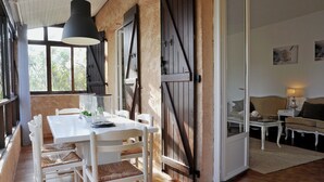 A dining area with a white table and chairs, a hanging light fixture, and a view through a large window. - Villa in Frejus With Pool Near Beach (Fréjus)