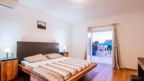 Un dormitorio con cama, cabecero de madera, mesitas de noche con lámparas, vista a través de un ventanal y una pequeña fotografía en la pared.