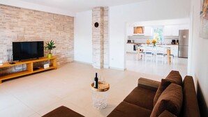Una sala de estar moderna con televisor de pantalla plana, un sofá marrón y una zona de comedor con una cocina al fondo.