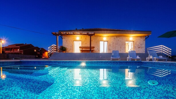 Una piscina con suelo de baldosas, un edificio de fachada de piedra y mobiliario exterior.