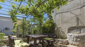 Un espacio al aire libre con mesas y bancos de madera, rodeado de vegetación y un muro de piedra.