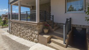 Un edificio de dos pisos con fachada de piedra, un porche cubierto con barandilla y una escalera que conduce a la entrada.