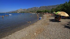 Una playa con agua cristalina, orilla pedregosa y montañas al fondo.