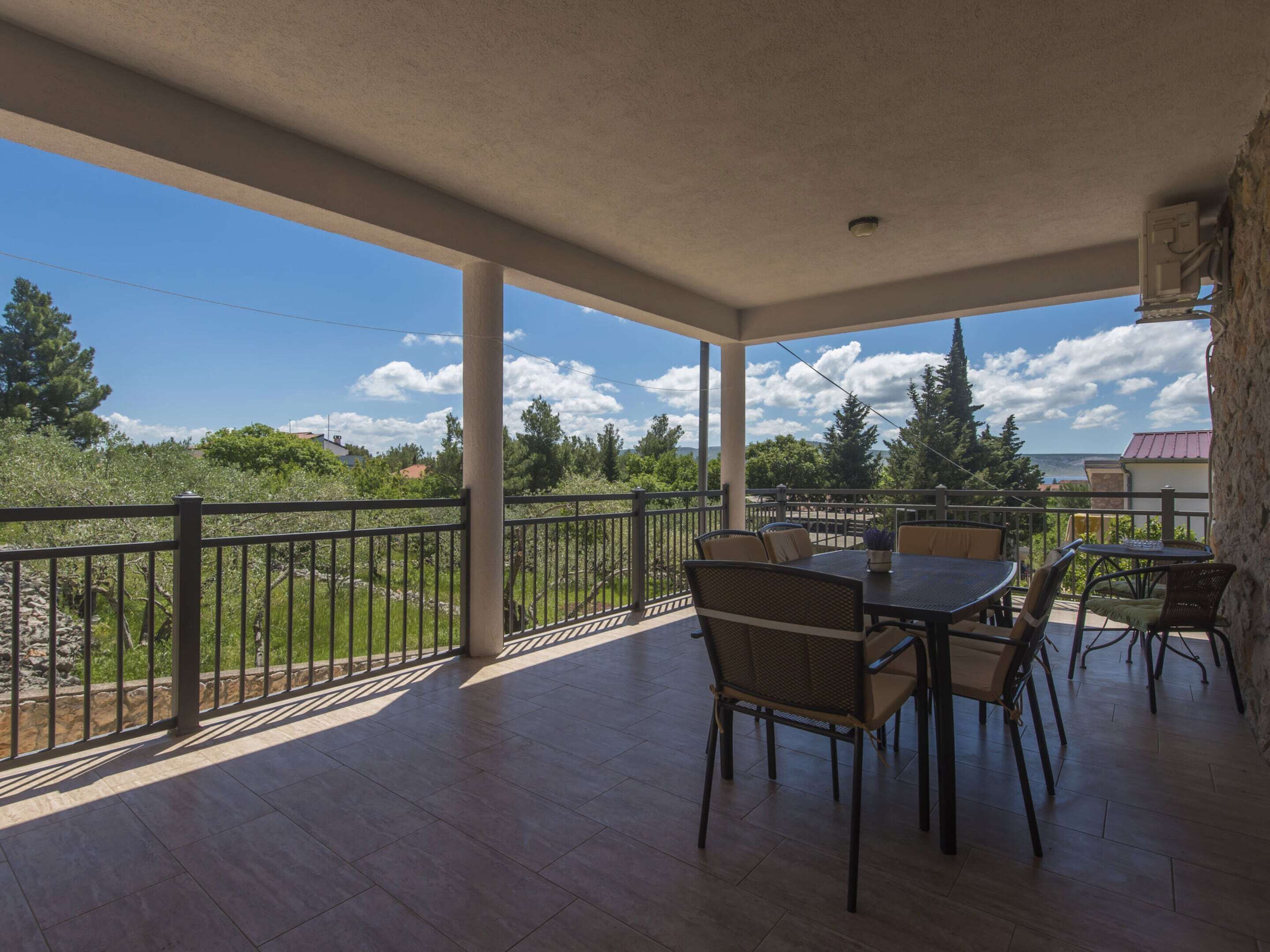 A covered patio with a table and chairs, a stone wall, and a view of trees and a body of water.
