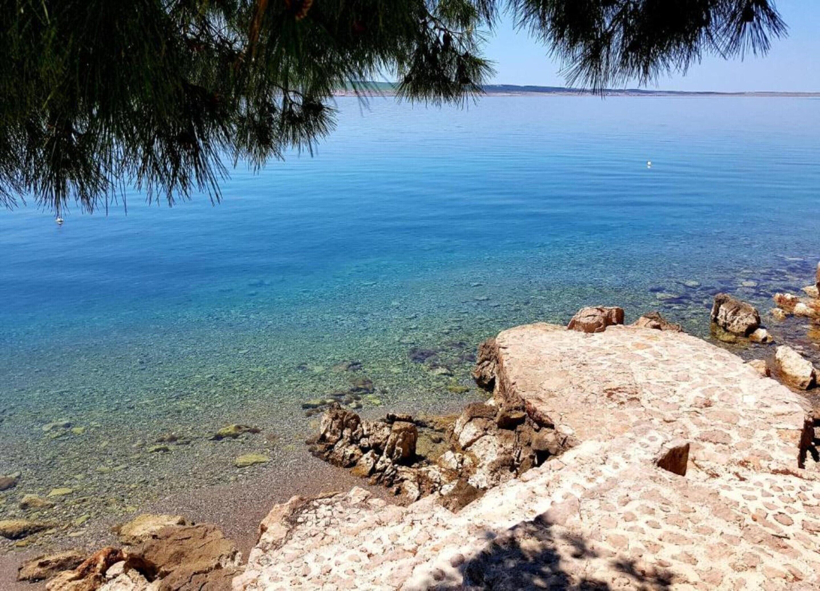Paesaggio costiero con acque limpide, una riva rocciosa e una terraferma in lontananza.