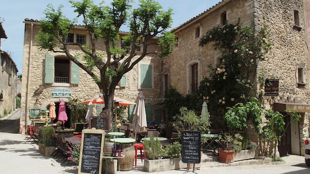 Un bâtiment rustique en pierre abritant un café appelé « Le Petit Café », avec une terrasse et de la verdure.