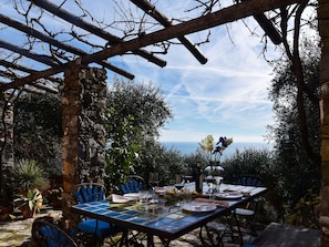 Un espacio de comedor al aire libre con pared de piedra, sillas azules y una mesa dispuesta para dos.
