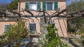 Une maison avec un mur en pierre, une table mise pour le repas et un jardin avec des arbres et des plantes.