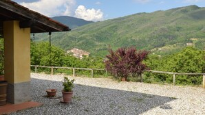 A building with a gravel patio, potted plants, and a view of a mountainous landscape. - Beautiful Cottage in Pescia with Hot Tub (Pescia)