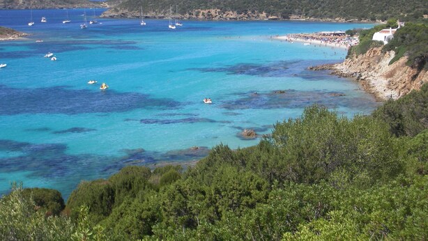 Une zone côtière aux eaux turquoise et limpides, avec des bateaux et une plage où se trouvent des gens.