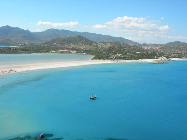 A coastal landscape with a clear blue sea, a sandy beach, and distant mountains. - Belvilla by OYO Mura Pranu (Sant'Antioco)
