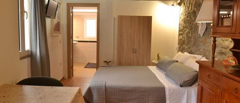 A bedroom with a bed, a wooden wardrobe, a desk, and a chair.