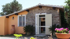 Un bâtiment en pierre doté d’une porte et de fenêtres, entouré de plantes en pot et bordé d’un chemin de gravier.