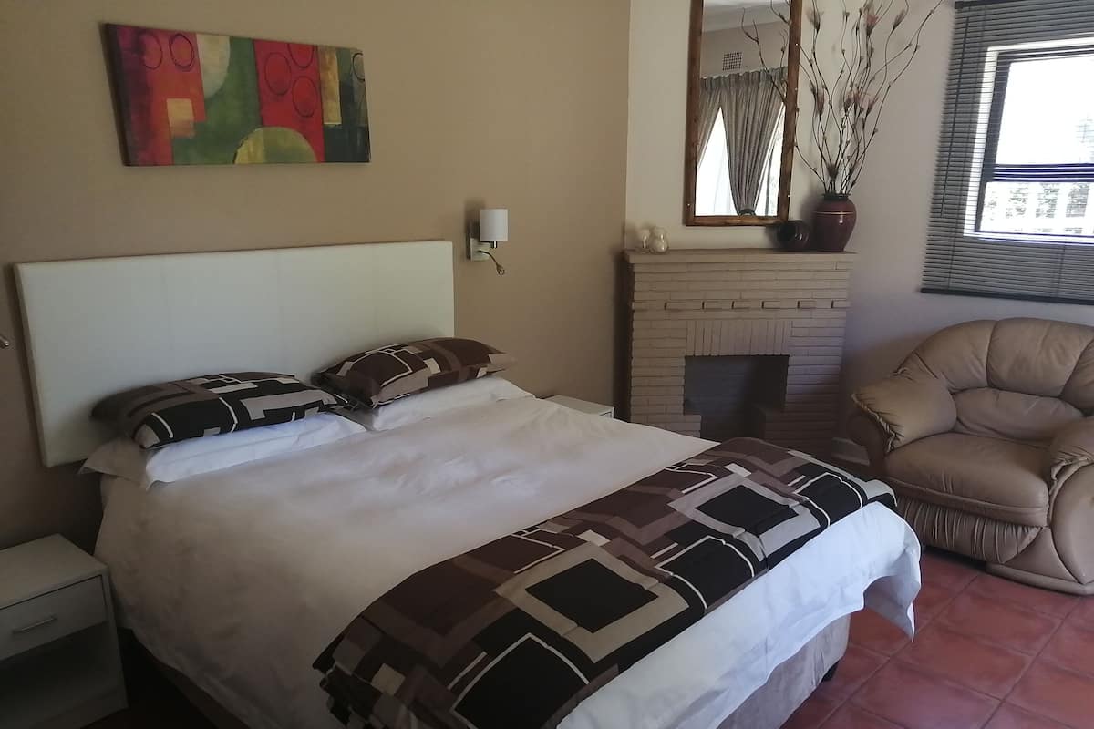 Ein Hotelzimmer mit einem großen Bett, einem Kopfteil, einem Nachttisch, einer Wandlampe, einem Kamin, einem Sessel und einem Fenster mit Jalousien.