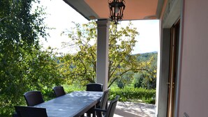 An outdoor patio with a table and chairs, surrounded by greenery and a view of hills. - House in Pistoia Countryside (Pistoia)