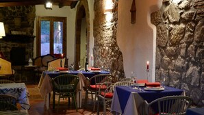 A cozy restaurant with stone walls and wooden beams, featuring tables set for dining with chairs.